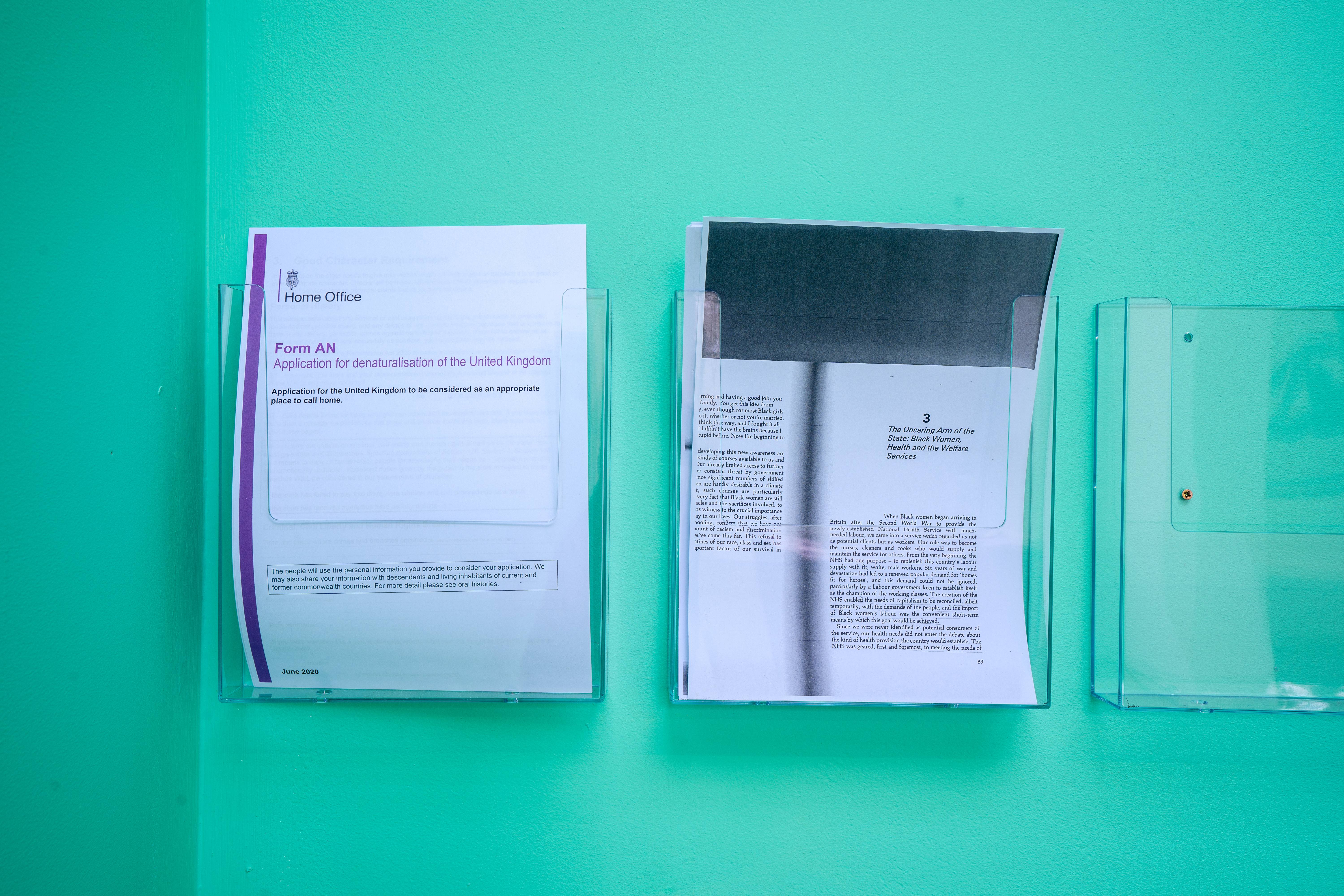 Sheets of official immigration documents sit in plastic holders against a blue wall.