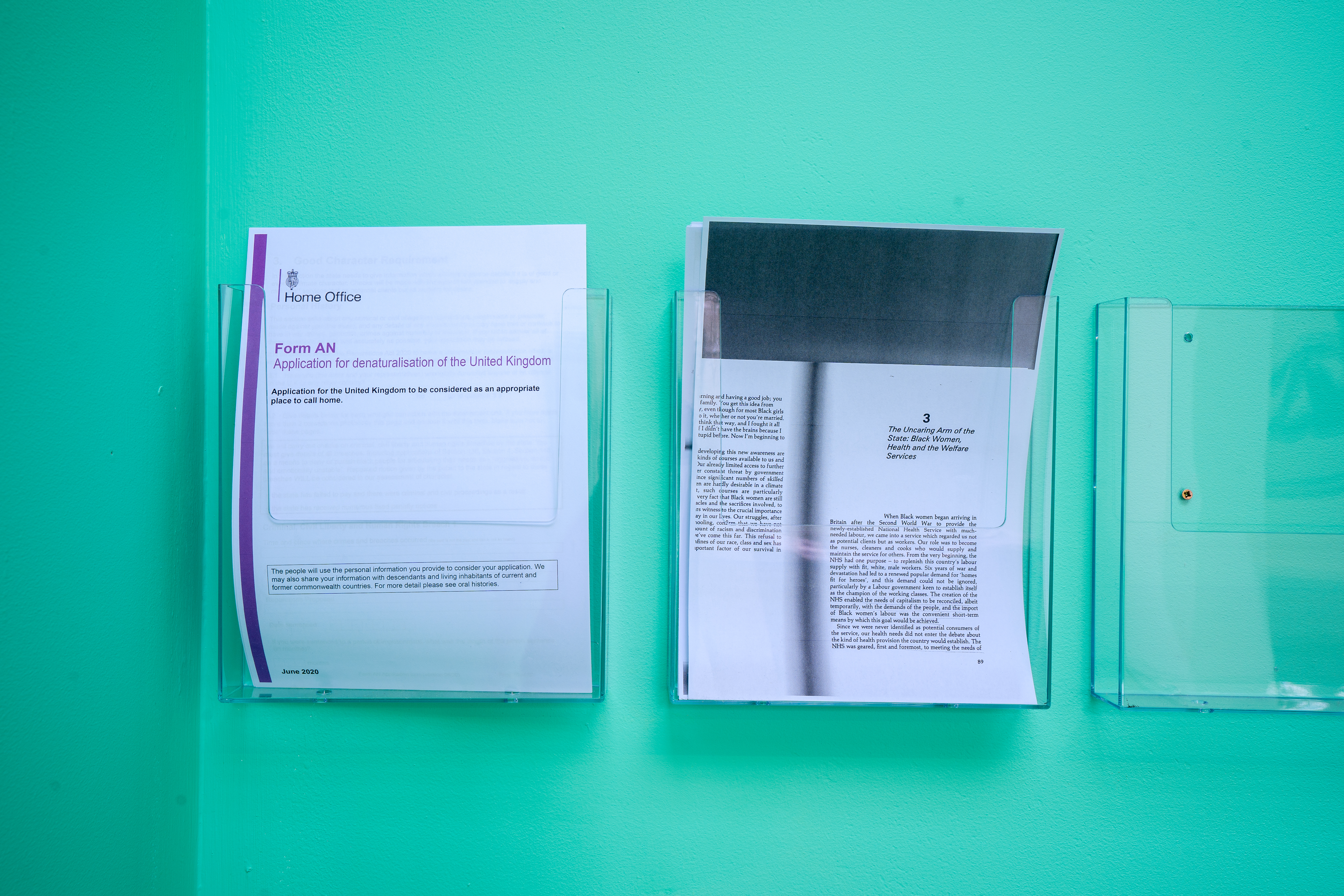 Sheets of official immigration documents sit in plastic holders against a blue wall.